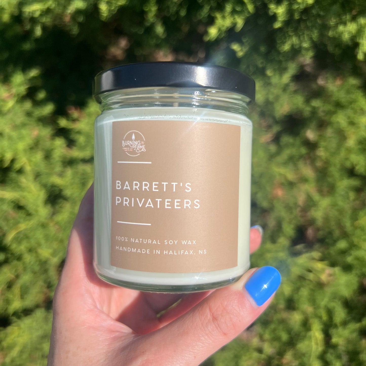 Hand holding a candle labeled 'Barrett's Privates' against a green outdoor background