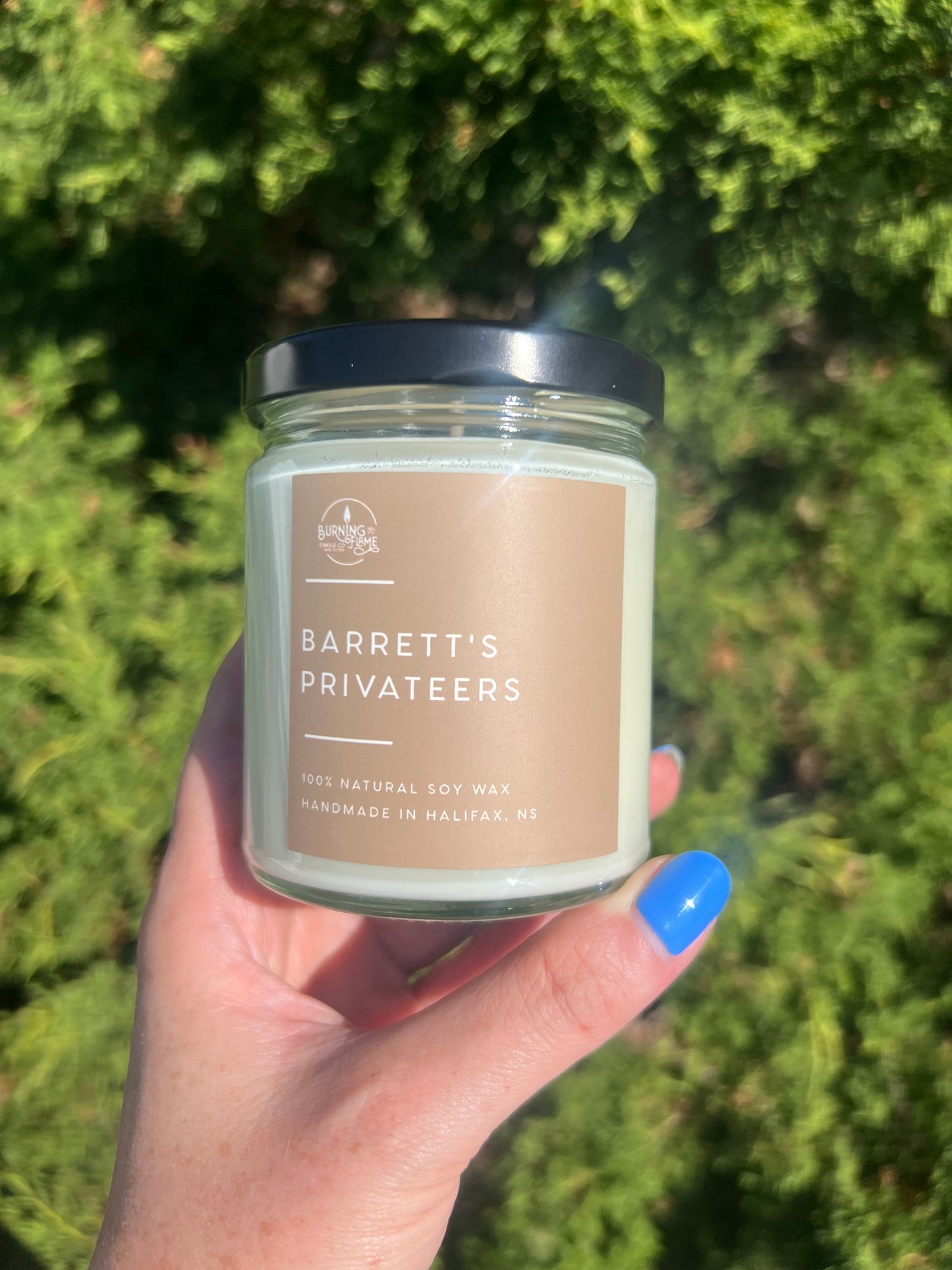Hand holding a candle labeled 'Barrett's Privates' against a green outdoor background