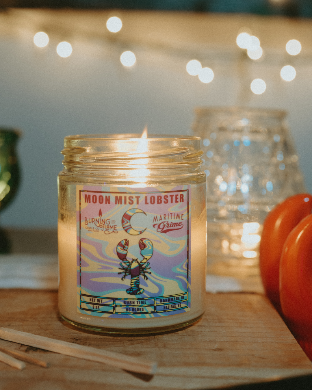 Soy candle with Moonmist label on a wooden surface with blurred lights in the background